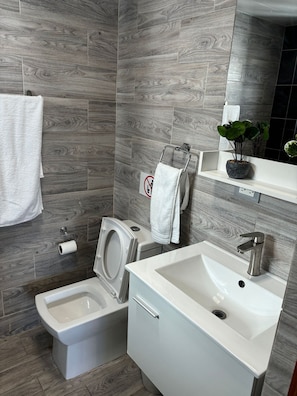 A modern bathroom with a grey wood-textured wall, a white sink, a toilet, and a bidet. - Penthouse Ejecutivo Santo Domingo  (Santo Domingo)