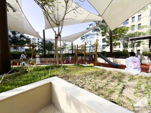 Explore the playground area with a slide and climbing elements, surrounded by trees and a low wall.