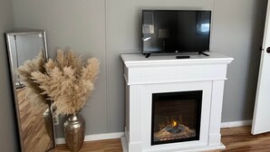 Een woonkamer met een witte open haard, een flatscreen televisie erboven en een lijst met een foto links.