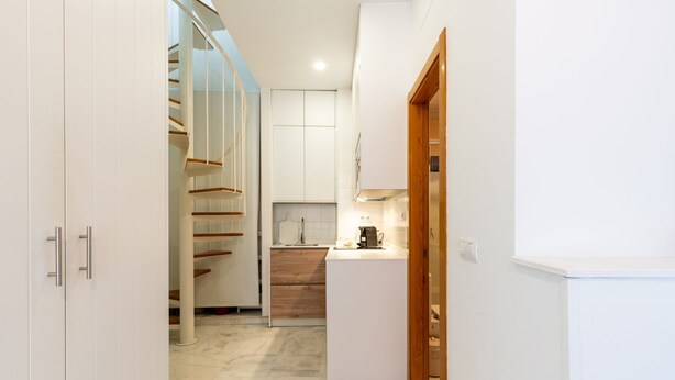 Un pasillo estrecho que conduce a una cocina con una escalera de madera y una puerta blanca.