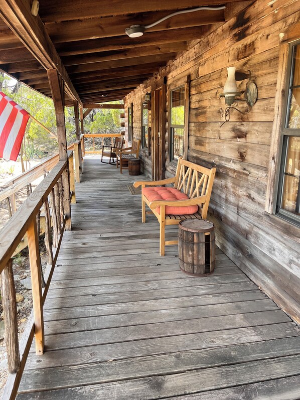 A wooden porch with a bench and chairs, a small table, and a decorative wall-mounted light fixture. - Cedar Ridge Log Cabin on 14 acres - Pet Friendly! (Granbury)