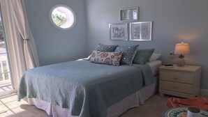 Quarto com cama, mesa de cabeceira, abajur e janela com cortinas.