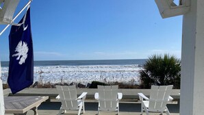 A wooden deck with white chairs and a flag, overlooking a beach with waves. - Stunning Oceanfront Home with Private Beach Access - 468 Tarpon (Fripp Island)