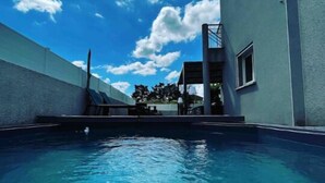 Una piscina con agua azul cristalina, rodeada por un edificio moderno de fachada blanca y un ventanal pequeño.