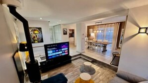 Una sala de estar moderna con un televisor de pantalla plana, un sofá, una mesa de centro y un comedor al fondo.