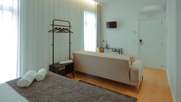 Habitación de hotel con cama, mesita de noche, espejo, perchero, una pequeña mesa con lámpara y televisión en la pared.