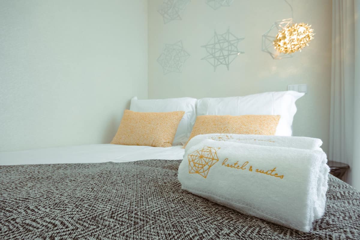 Ein ordentlich bezogenes Bett mit weißen und gemusterten Kissen, einer strukturierten Decke und einem Handtuch mit geometrischem Muster.