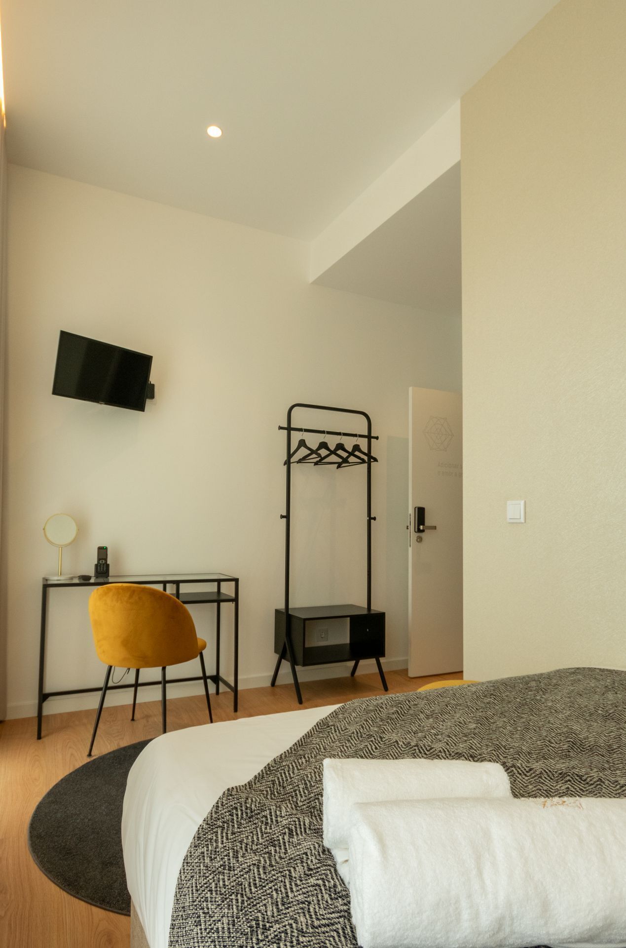 A hotel room with a bed, a desk with a chair, a coat rack, and a television mounted on the wall.