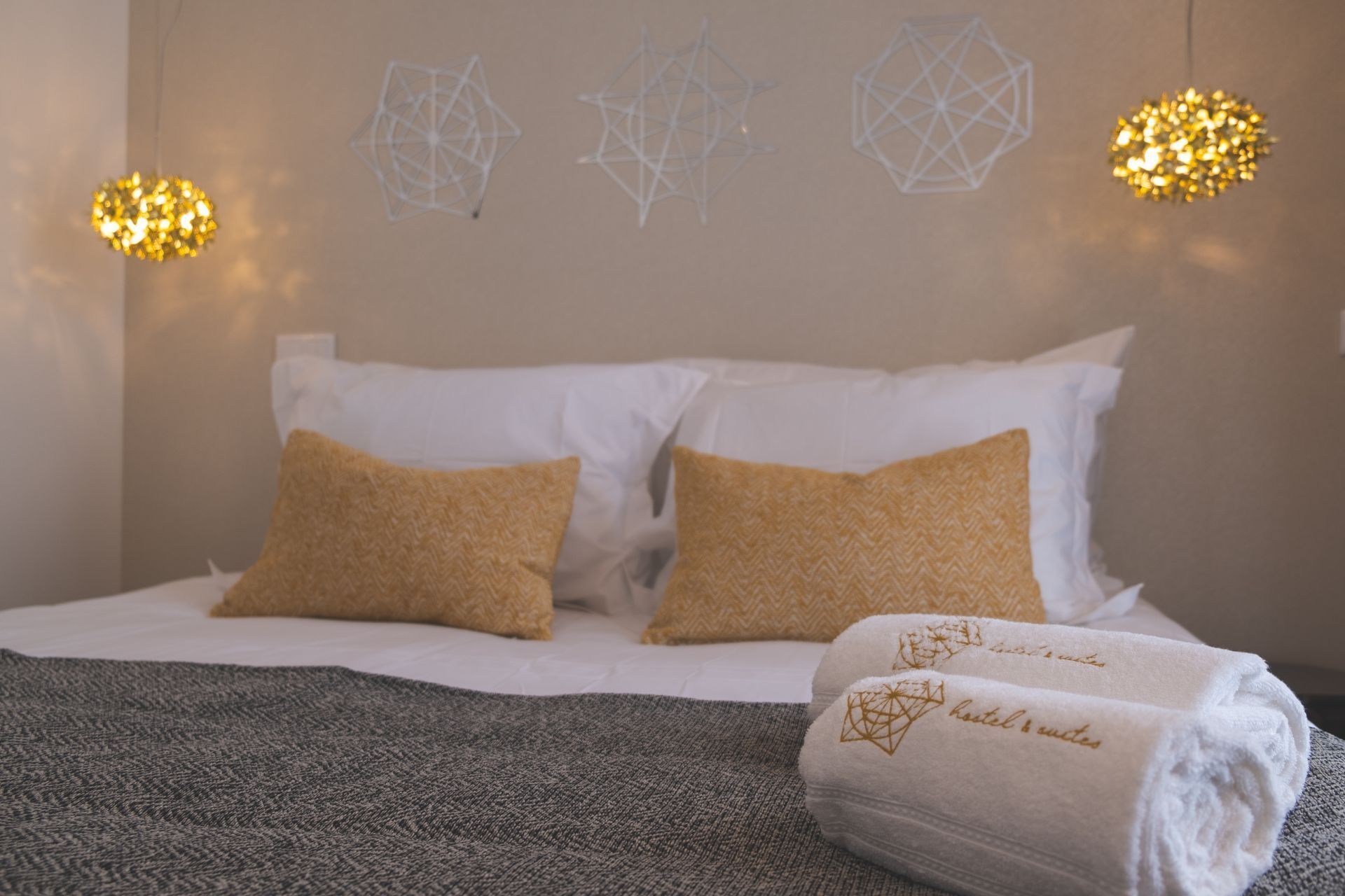 A neatly made bed with white and beige pillows, a grey textured blanket, and a folded towel with a geometric design.