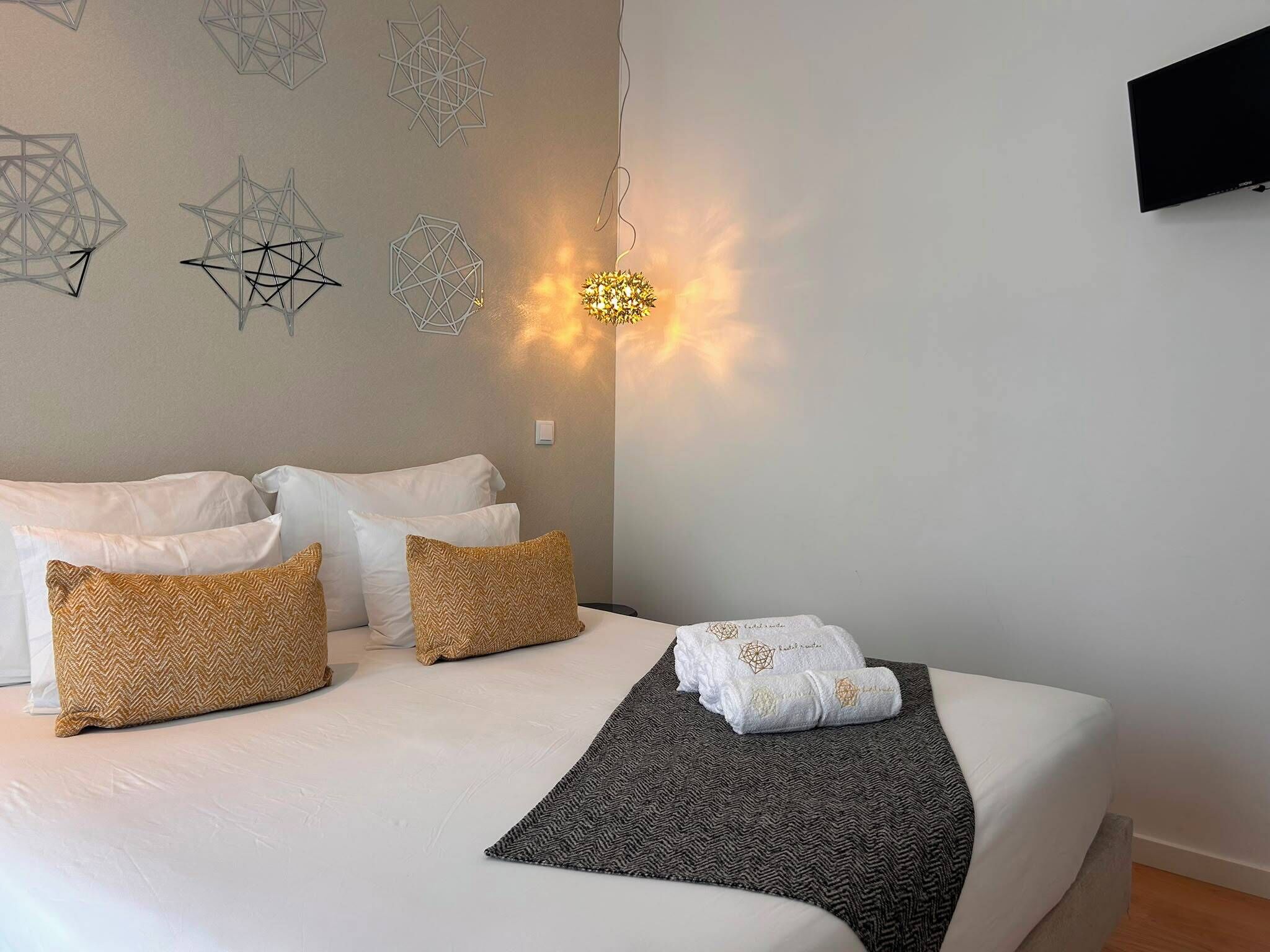 A hotel room with a bed, pillows, a blanket, and wall art.