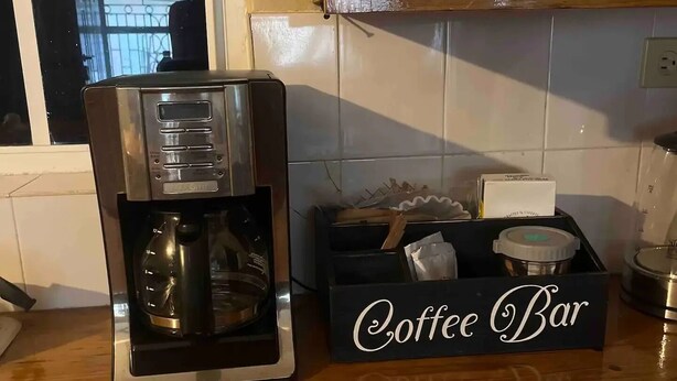 A kitchen counter with a coffee maker, a coffee bar box, and stacked plates and cups. - Prime Negril Location - 2br brand new apartment. New Water tank installed. (Negril)