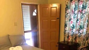 A bedroom with a bed, a nightstand, a chair, and a door. - Prime Negril Location - 2br brand new apartment. New Water tank installed. (Negril)