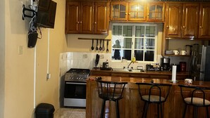 A kitchen with wooden cabinets, a stove, a sink, and a dining area with stools. - Prime Negril Location - 2br brand new apartment. New Water tank installed. (Negril)