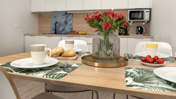 Une table à manger dressée avec des assiettes, des tasses et un vase de fleurs.