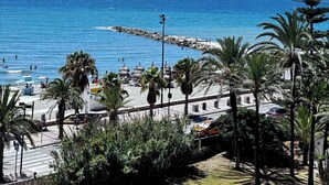 A coastal view with a clear sky, a rocky breakwater, and palm trees. - Beautiful Place With Endless sea View (Fuengirola)