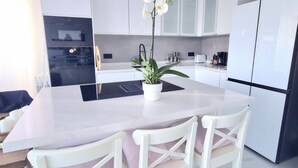 A modern kitchen with white cabinetry, a central island with a plant, and a built-in oven. - Beautiful Place With Endless sea View (Fuengirola)