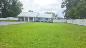 A house with a covered porch, a well-maintained lawn, and a white fence. - Charming & Cozy 3bdr 2b Home in Heart of Swansboro Perfect for a Relaxing Stay! (Swansboro)