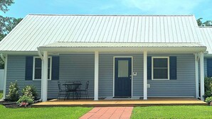 Ein Bungalow mit überdachter Veranda, Eingangstür und einem kleinen Tisch mit Stühlen.