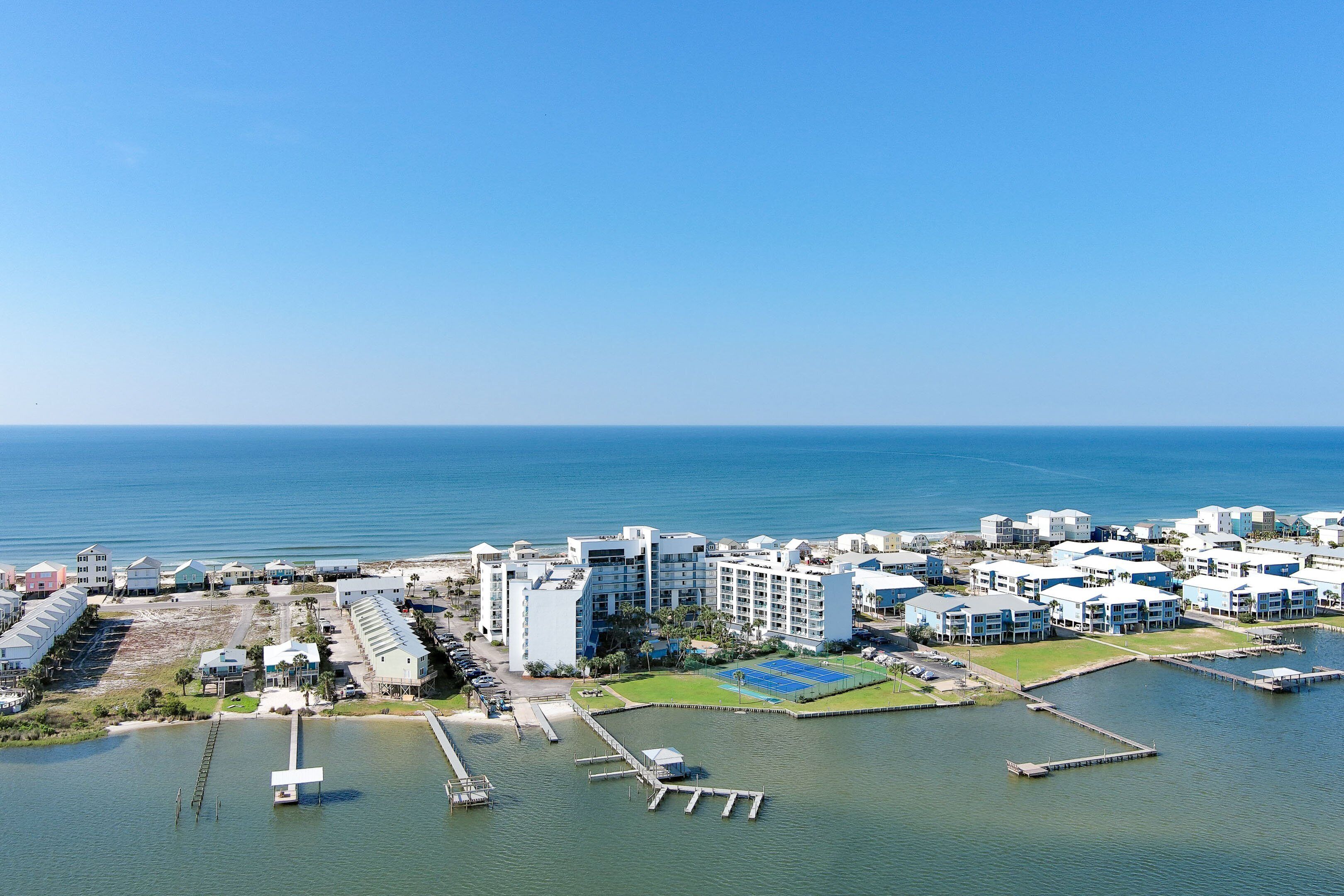An aerial view of a coastal hotel complex with multiple buildings, a marina, and a tennis court.
