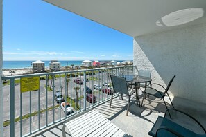 Een balkon met uitzicht op het strand en de parkeerplaats.