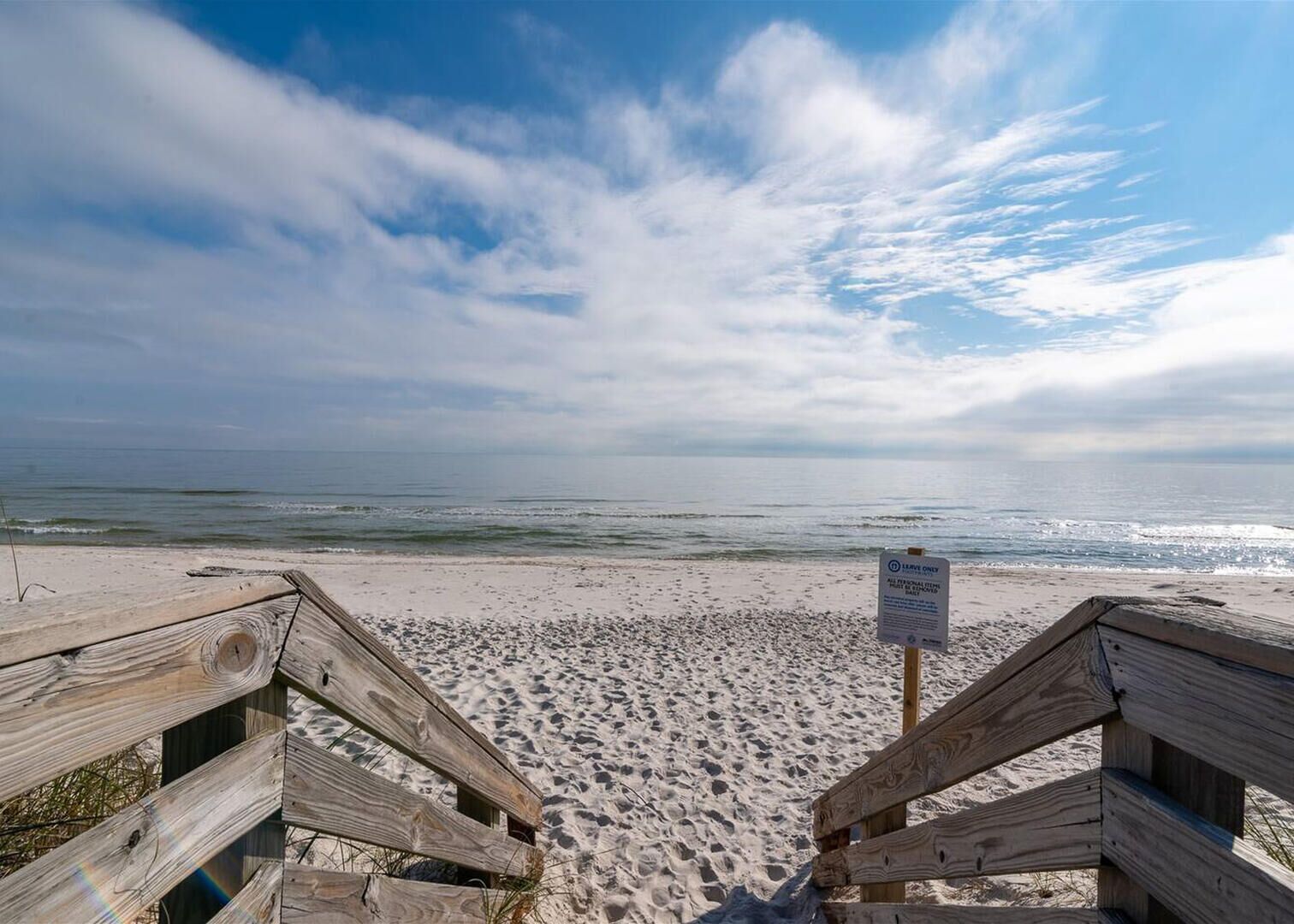 Un muelle de madera que lleva a una playa con un cartel que dice 'Leave Only Trash'.