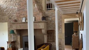 Un amplio salón con pared de piedra, vigas de madera en el techo y chimenea.