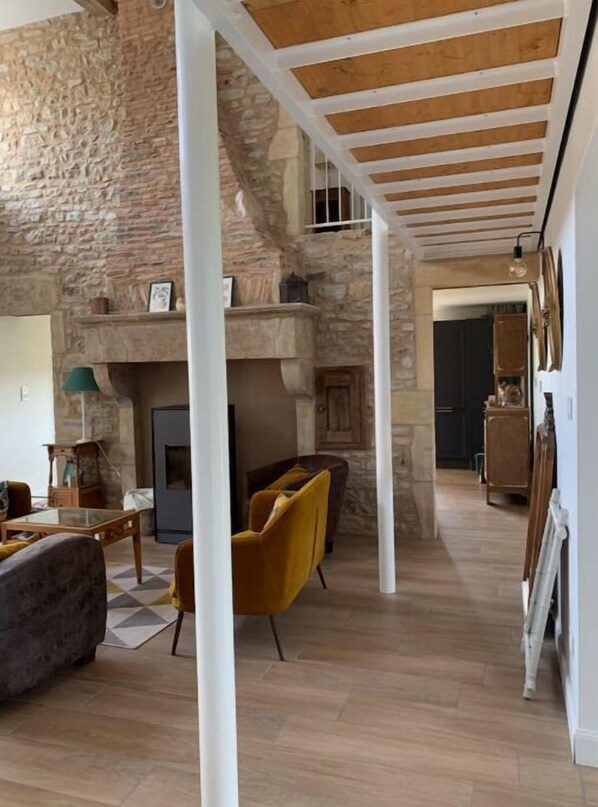 Un amplio salón con pared de piedra, vigas de madera en el techo y chimenea.
