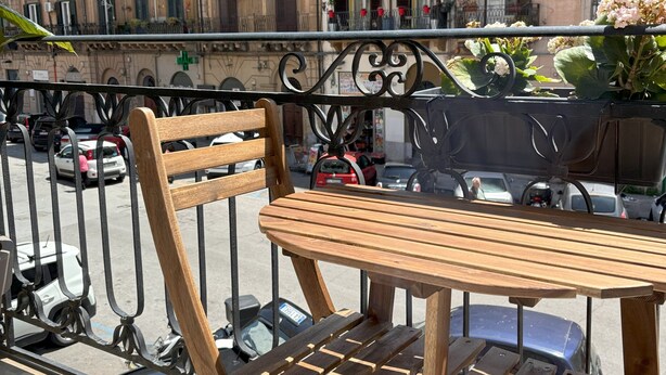Une table et une chaise en bois sur un balcon donnant sur une rue et des immeubles.