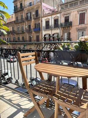 Une table et une chaise en bois sur un balcon donnant sur une rue et des immeubles.
