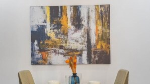 A dining table with two chairs, a vase with flowers, and a painting on the wall.