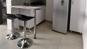 Cozinha moderna com armários brancos, uma geladeira de aço inoxidável, um micro-ondas e dois banquetas.