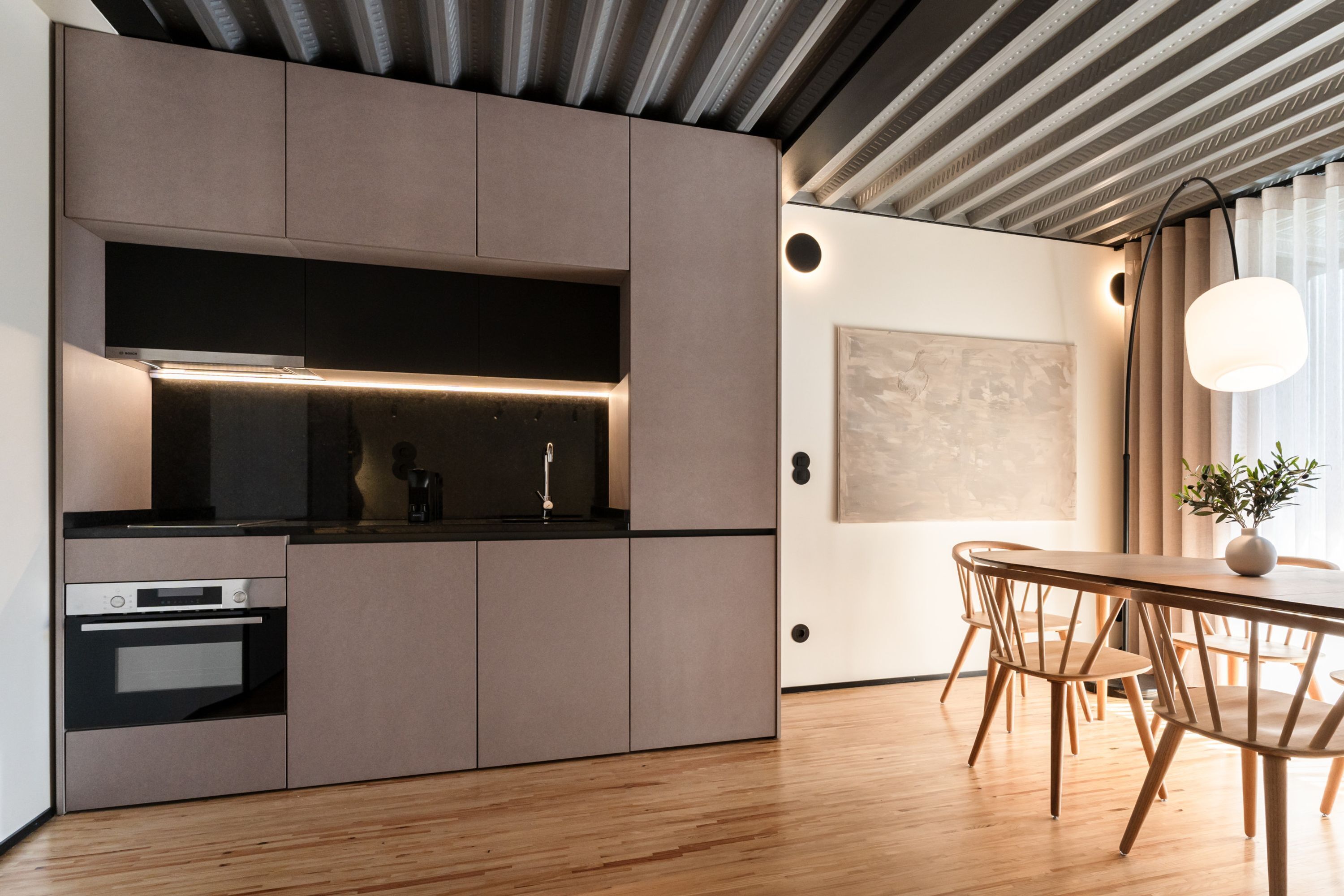 Una cocina moderna con electrodomésticos integrados, un comedor con muebles de madera y un amplio ventanal con cortinas.
