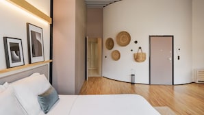 A modern hotel room with a curved wall, a bed with white linens, a wooden floor, and a door with a handle. - Feel Porto Matosinhos City Flat III (Matosinhos)