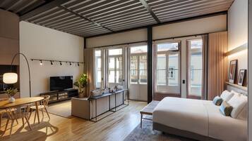Habitación de hotel moderna con suelo de madera, una cama, un escritorio, un televisor y ventanas amplias.