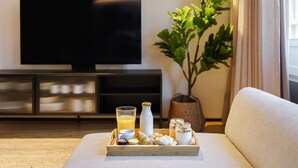 A living room with a flat-screen TV, a sofa, a tray with breakfast items, and a potted plant. - Feel Porto Matosinhos City Flat III (Matosinhos)
