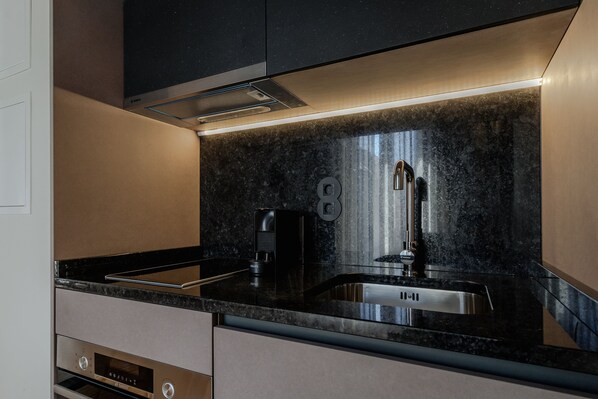 A modern kitchen with a black countertop, stainless steel sink, and built-in oven.