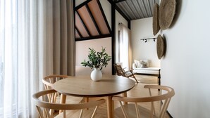 A dining area with a round wooden table and chairs, a white vase with a plant, and a wall with woven decor. - Feel Porto Matosinhos City Flat V (Matosinhos)