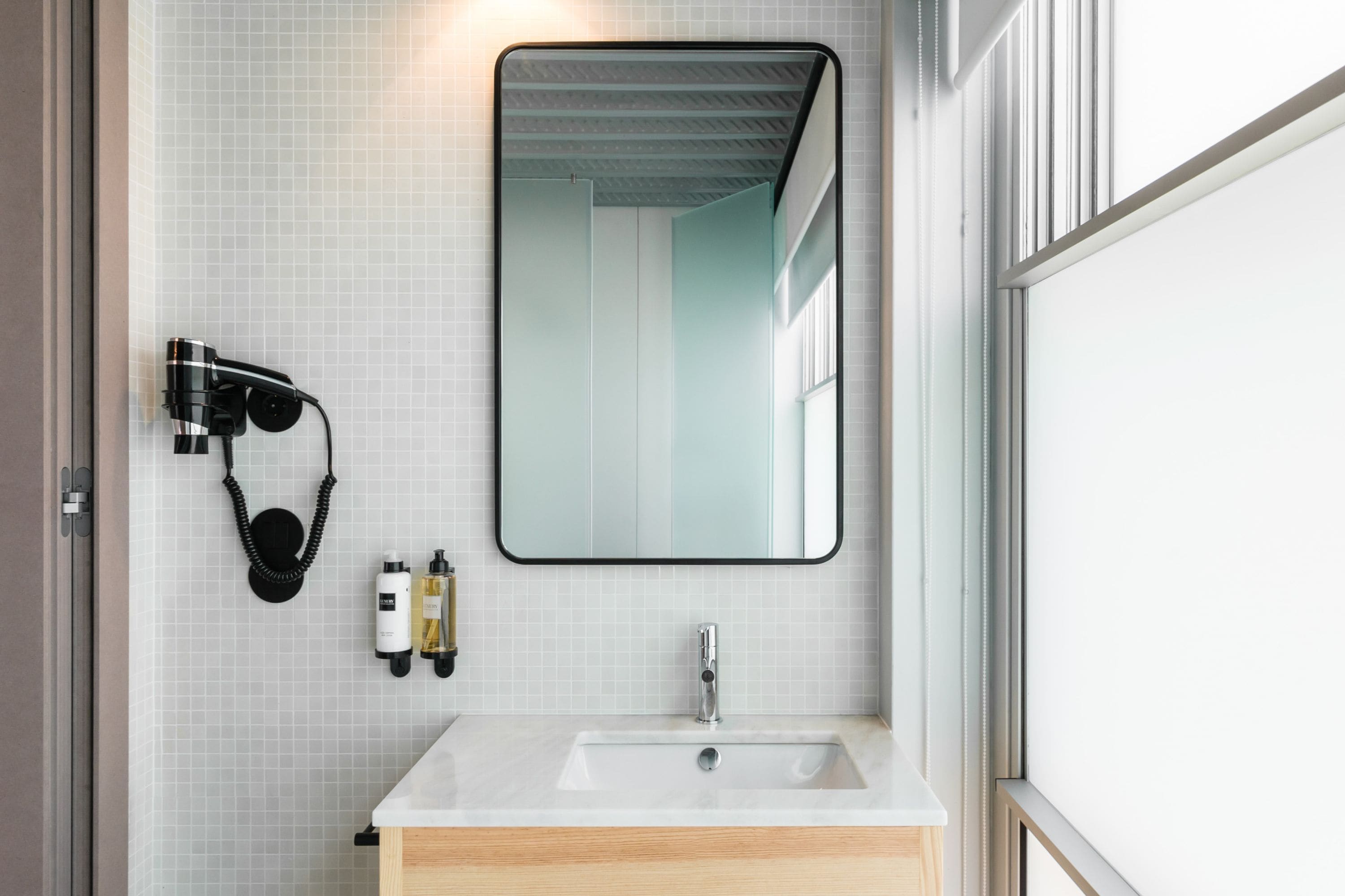 Une salle de bain moderne avec un lavabo blanc, un grand miroir et un sèche-cheveux fixé au mur.