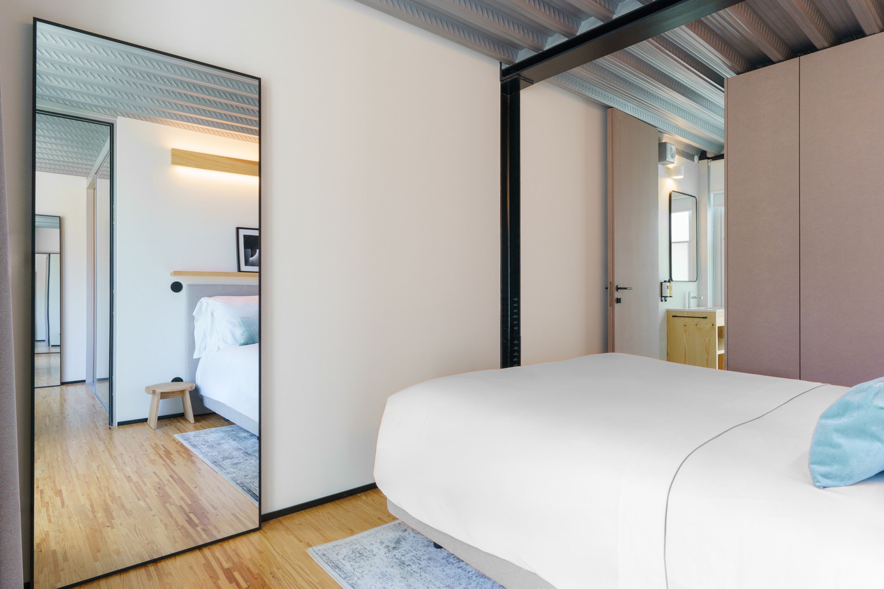 Une chambre à coucher avec un lit, un petit tabouret, un miroir et un plancher en bois.