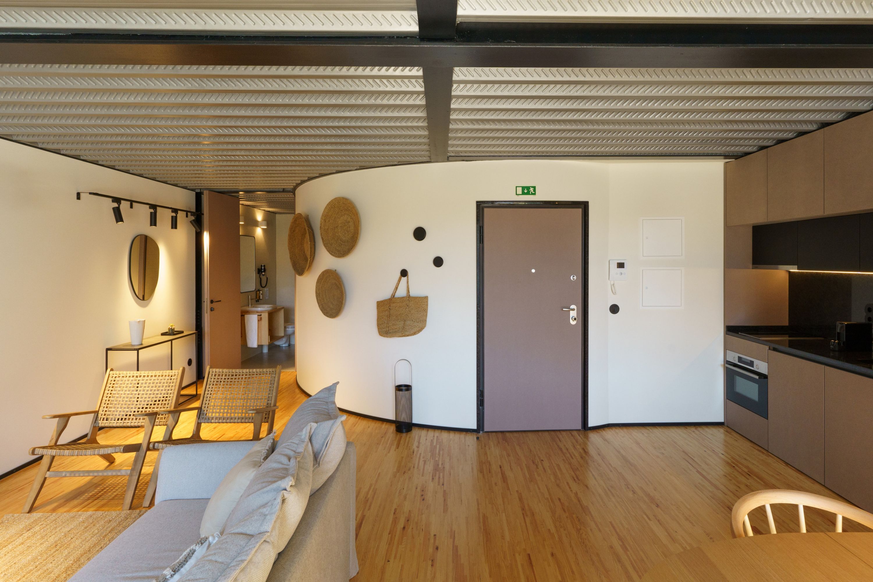 A modern interior with a curved wall, a kitchenette, a seating area with a sofa and chairs, and a door with an emergency exit sign.