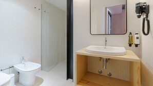 Une salle de bain moderne avec un lavabo blanc, un bidet, une douche en verre et un miroir équipé d’un sèche-cheveux.