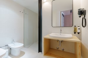Une salle de bain moderne avec un lavabo blanc, un bidet, une douche en verre et un miroir équipé d’un sèche-cheveux.