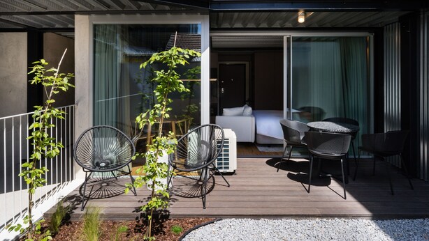 Un patio extérieur moderne, avec un canapé et des fauteuils, un petit arbre et un climatiseur blanc.
