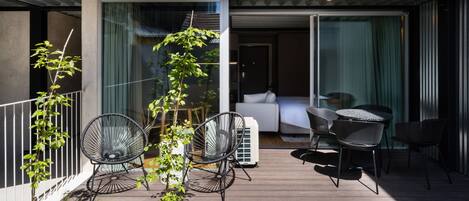 A modern outdoor patio with a sofa and chairs, a small tree, and a white air conditioning unit.