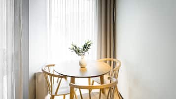 A round wooden table with four chairs, a white vase with a plant, and sheer curtains.