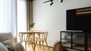 Ein modernes Wohnzimmer mit einer Couch, einem Esstisch mit Stühlen, einem Fernseher auf einem Schrank und einer Pflanze auf dem Tisch.