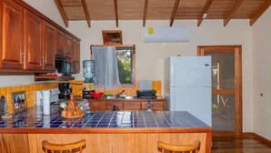 A kitchen with wooden cabinets, a tiled island, a refrigerator, and a window with a curtain. - Condo Caribbean Dreams (Dangriga)