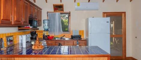 A kitchen with wooden cabinets, a tiled island, a refrigerator, and a window with a curtain.