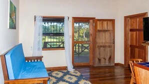A room with a wooden floor, a blue sofa, a wooden table, and a large wooden door. - Condo Caribbean Dreams (Dangriga)