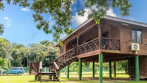 A wooden building with a balcony and a staircase leading to the entrance. - Condo Caribbean Dreams (Dangriga)